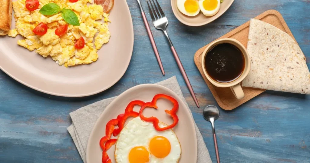 Pasture Raised Eggs: Cooking for Better Flavor & Nutrition 4 Breakfast spread featuring organic pasture raised eggs: scrambled eggs with cherry tomatoes and basil, sunny-side-up eggs with red bell pepper slices, boiled eggs, a cup of coffee, and a folded whole-grain tortilla on a blue wooden table.
