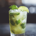 Mojito Mocktail Drink: A Fresh, Easy Sip Everyone Will Love 6 Homemade mojito mocktail drink in a tall glass, garnished with fresh mint leaves and a lime wedge, filled with crushed ice on a dark rustic table.