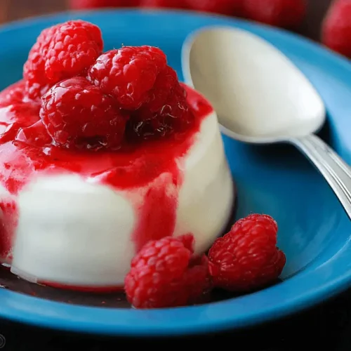 Easy Panna Cotta Recipe with Fresh Berry Sauce 3 Vibrant panna cotta with fresh raspberries and red sauce on a blue plate.